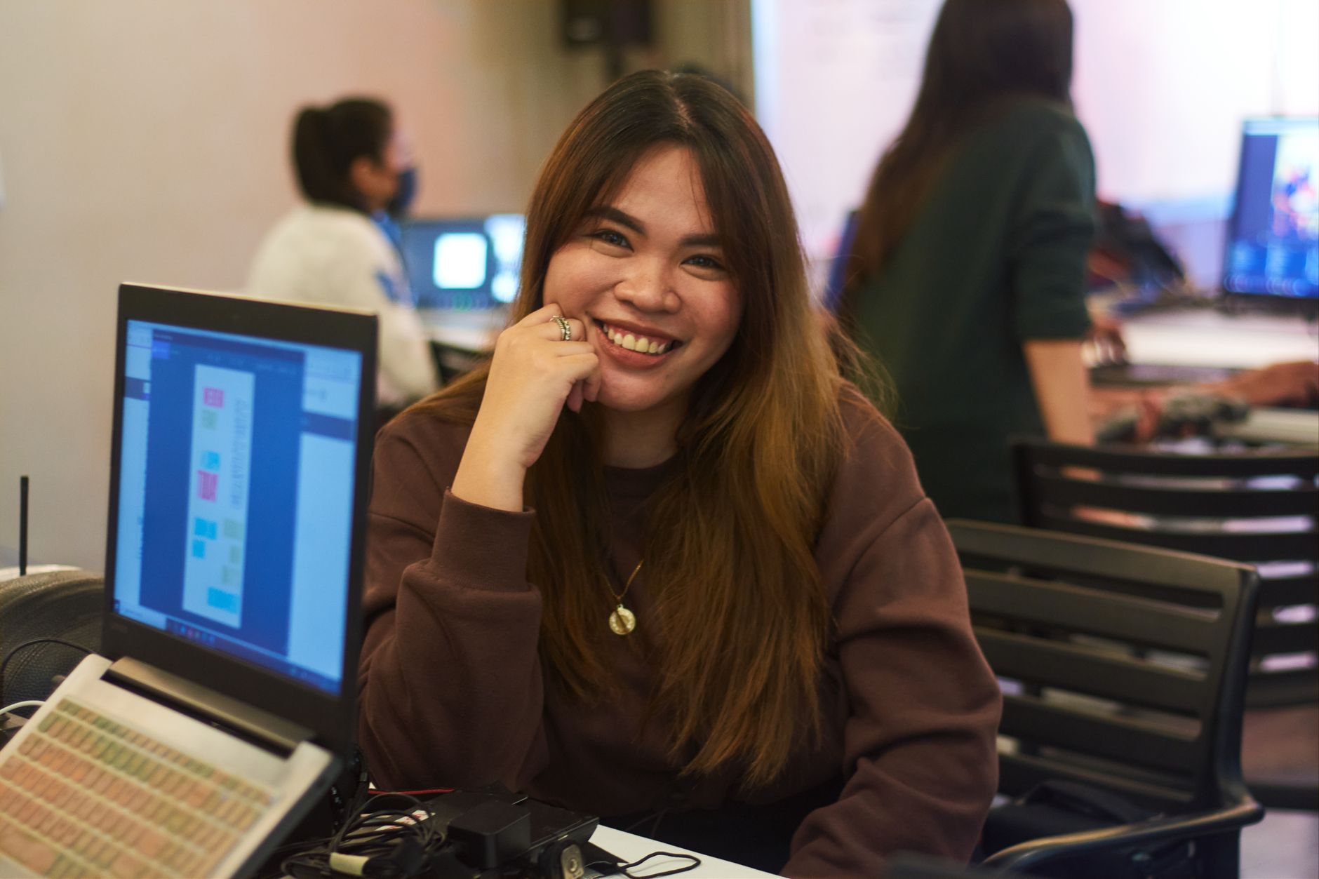 Femme asiatique souriante travaillant sur des ordinateurs portables dans un environnement de bureau animé.