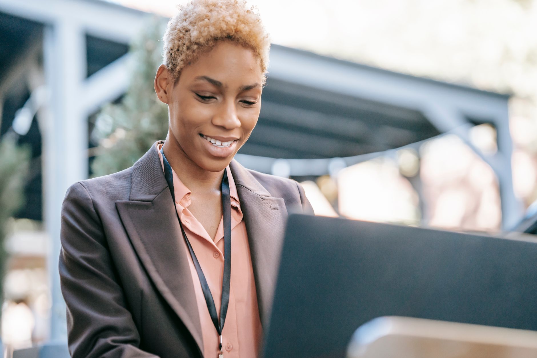 Femme afro-américaine positive en tenue formelle utilisant un ordinateur portable en extérieur, vue en contre-plongée.