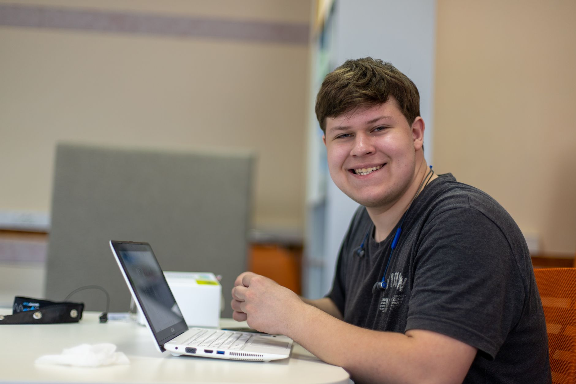 Jeune homme souriant travaillant sur un ordinateur portable dans un bureau moderne, ambiance détendue et productive.