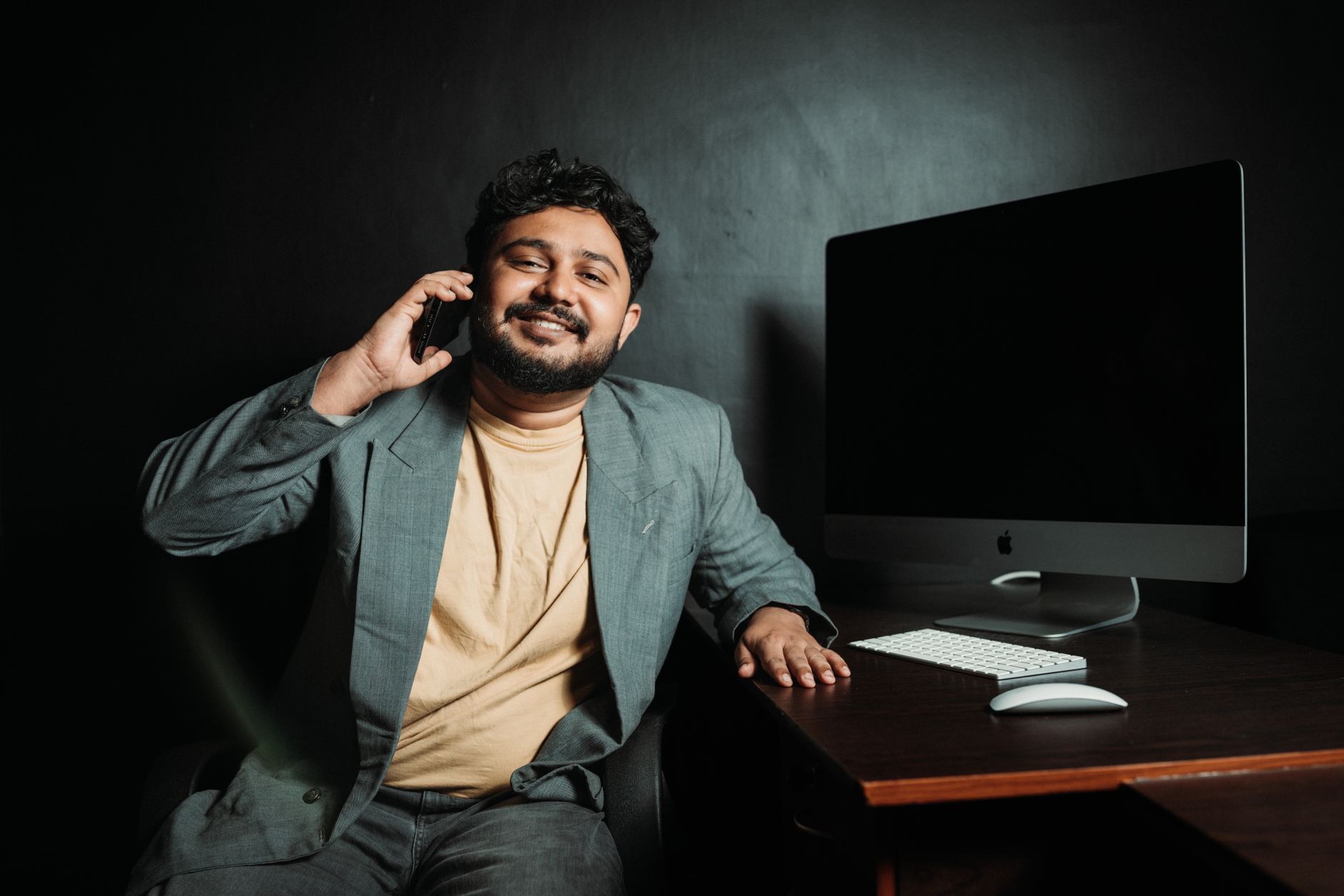 Homme d'affaires souriant au téléphone à son bureau devant un ordinateur.