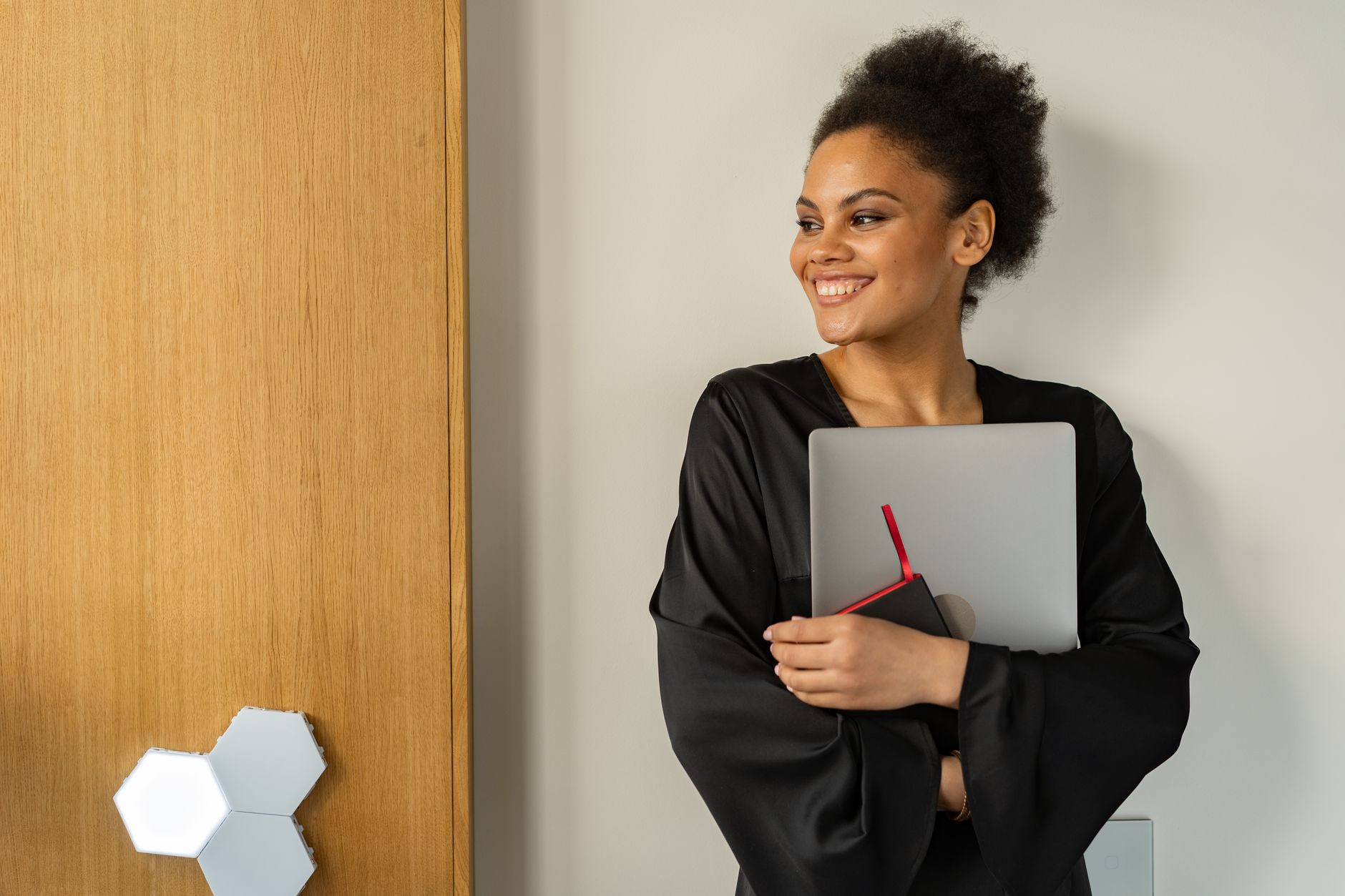 Femme souriante à la coiffure afro tenant un ordinateur portable en intérieur, dégageant confiance et positivité.