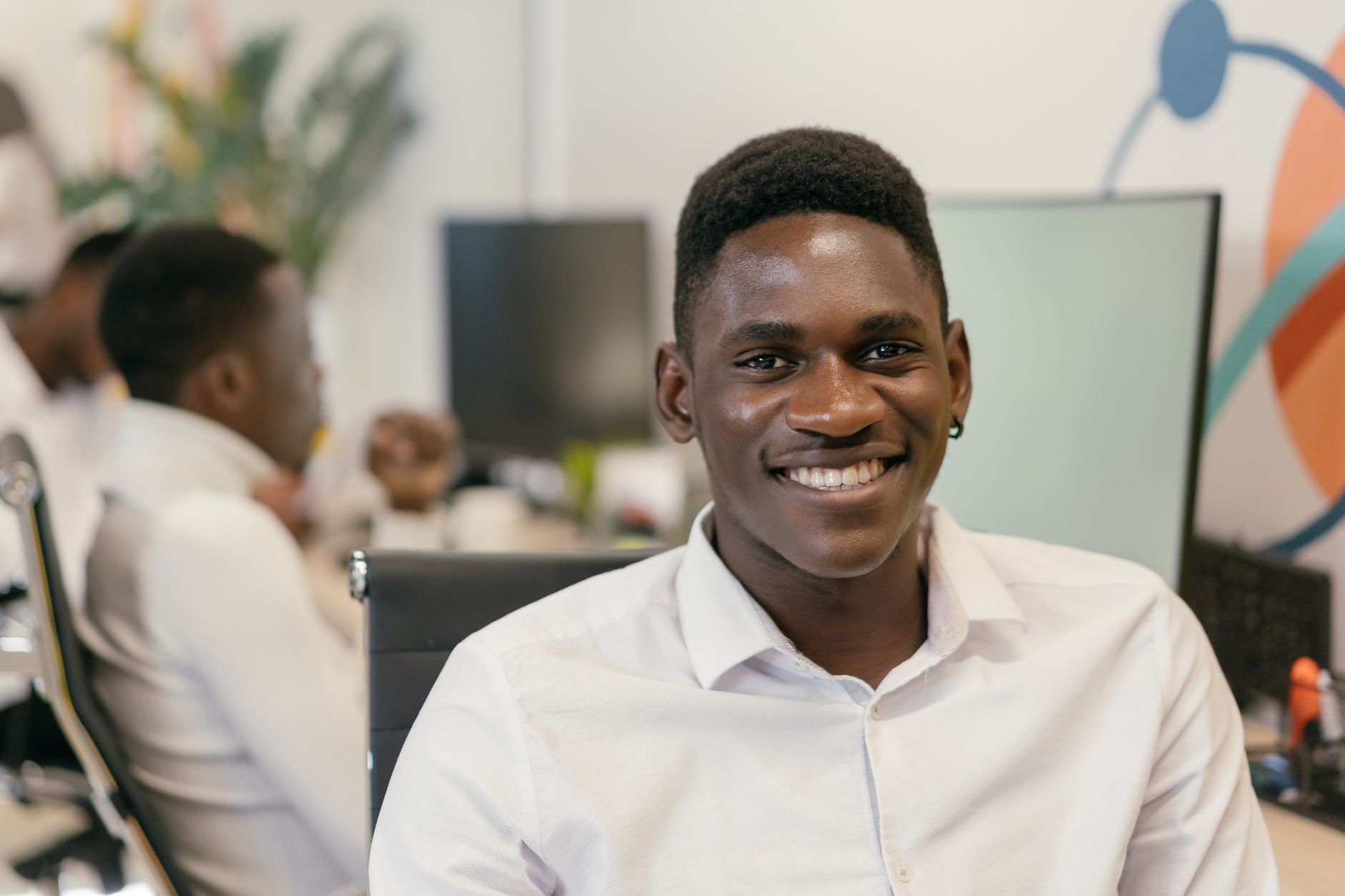 Jeune homme jovial en chemise blanche souriant à son bureau dans un environnement de bureau moderne.